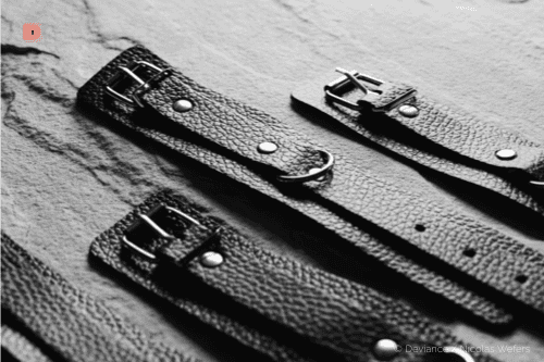Primer plano en blanco y negro de esposas de cuero negro con hebillas y anillas en D
