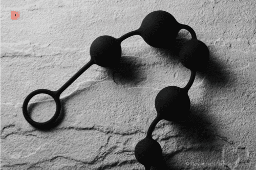 Primer plano en blanco y negro de un collar de bolas anales negro con anilla de tiro