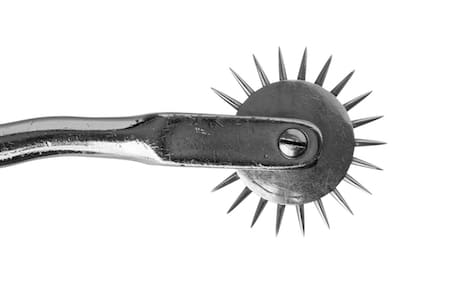 Primer plano de una rueda de Wartenberg sobre fondo blanco: un mango metálico con una rueda de púas giratoria