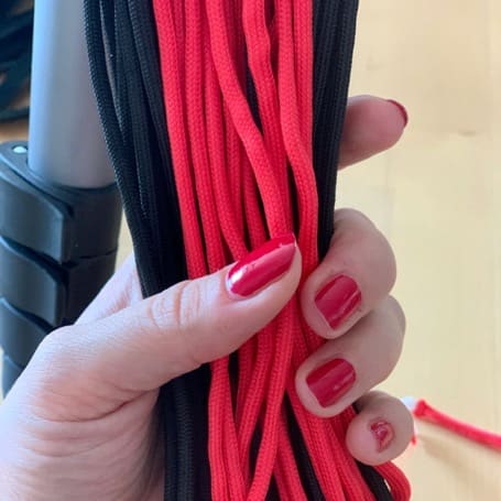 Una mano sujeta el haz cortado de cordones de paracord negros y rojos