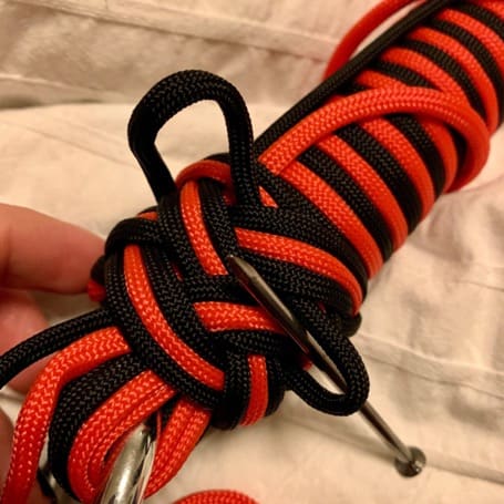 El trenzado de paracord negro y rojo se aprieta lazo a lazo con una aguja