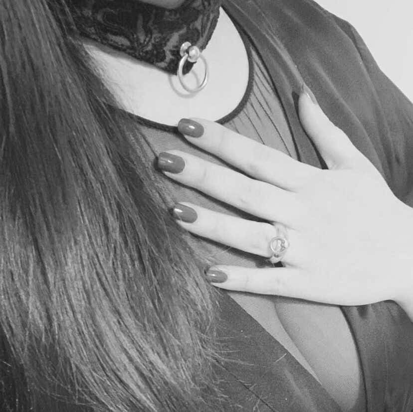 Primer plano en blanco y negro de una mano apoyada en el pecho sobre una blusa transparente, con un collar de encaje y anilla en O en el cuello