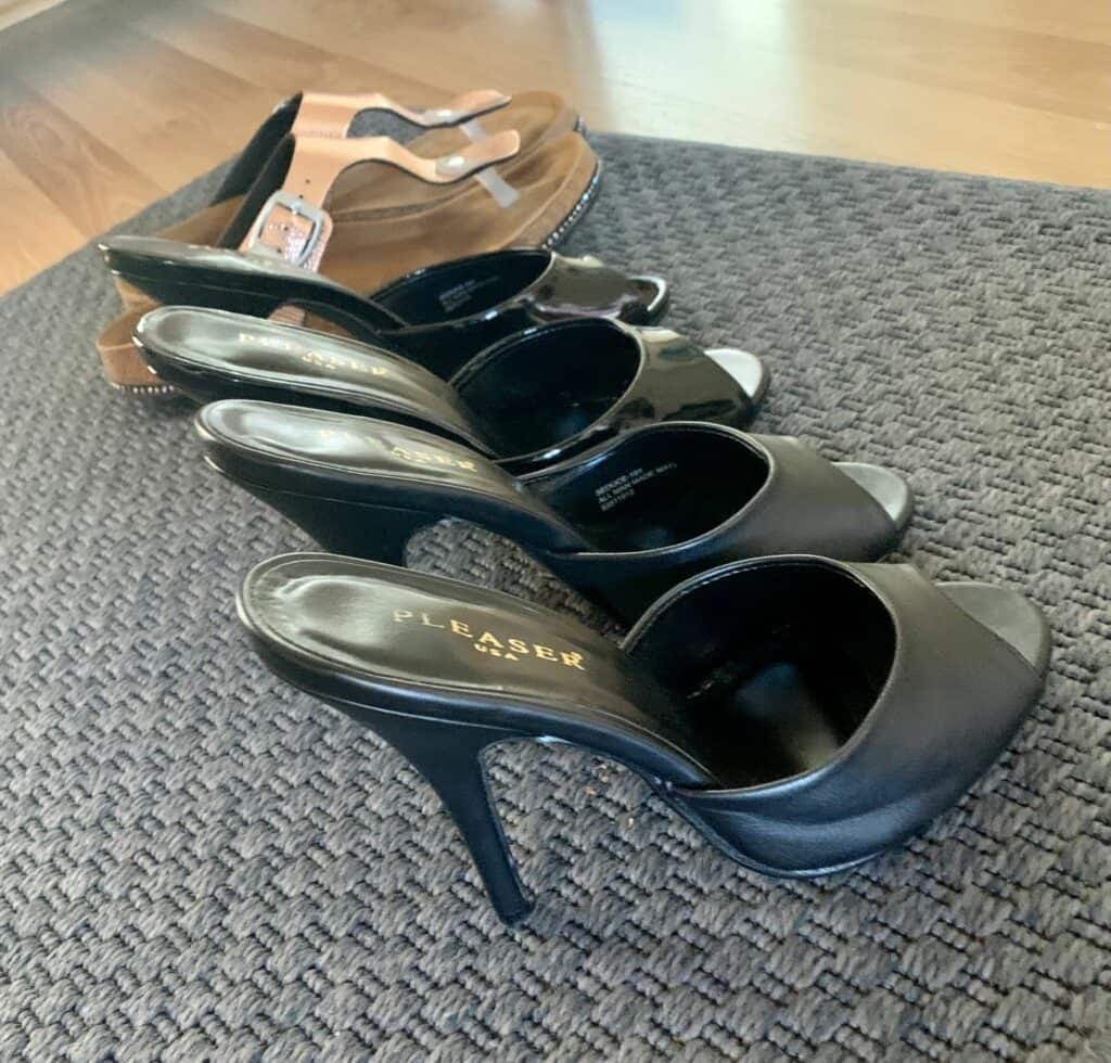 Cuatro pares de tacones y chinelas negros de la marca Pleaser alineados sobre una alfombra gris