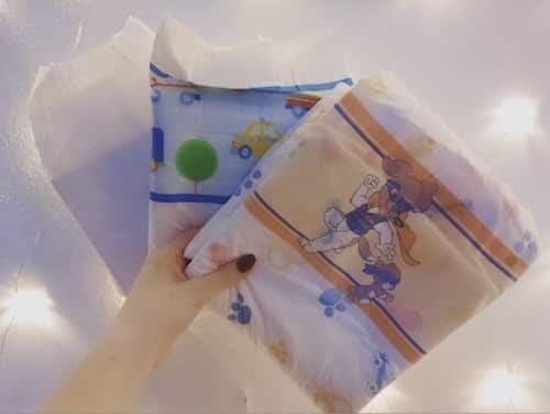 Una mano sostiene dos pañales estampados uno junto al otro, uno con coches y otro con perros