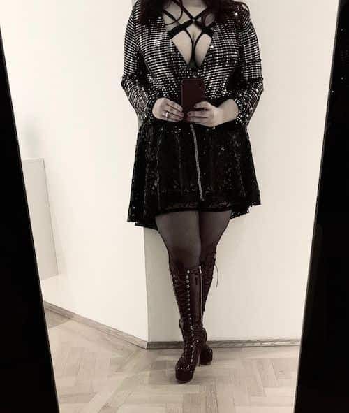 Selfie ante el espejo con chaqueta de lentejuelas, arnés negro, falda y botas altas de plataforma con cordones