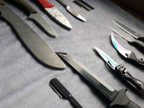 Una colección de cuchillos y hojas variados dispuestos uno junto a otro sobre una superficie gris