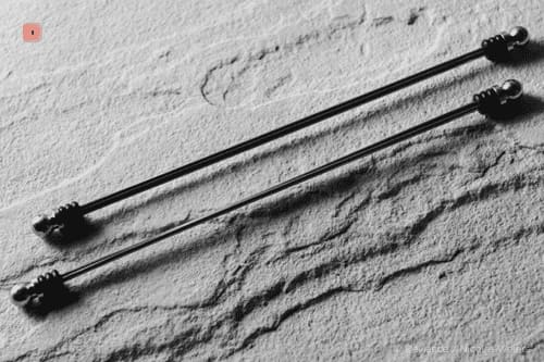 Fotografía en blanco y negro de dos pinzas para pezones de barra con extremos de bola, una junto a otra sobre piedra