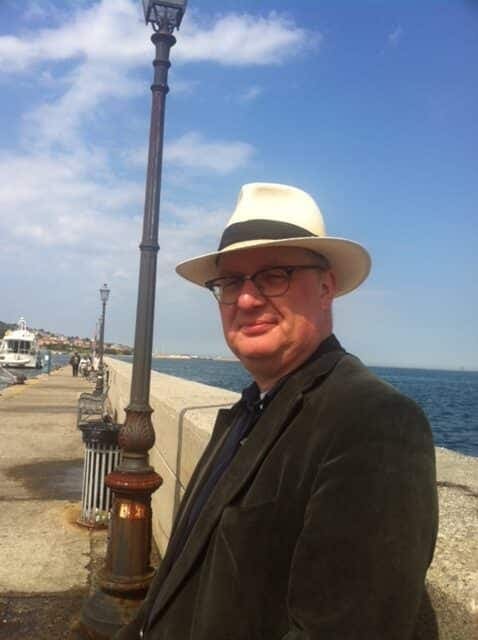 Retrato de un hombre con sombrero panamá, gafas y americana de terciopelo en un paseo portuario soleado
