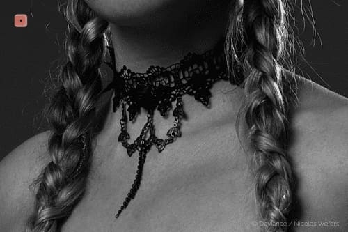 Primer plano en blanco y negro de un collar de encaje negro con flecos de cuentas en el cuello, entre dos trenzas