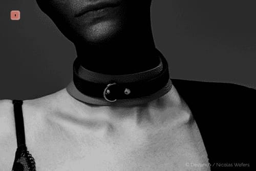 Primer plano en blanco y negro de un collar de cuero negro estrecho con una pequeña anilla en O