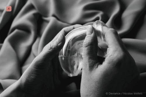 Primer plano en blanco y negro de dos manos sosteniendo un anillo de silicona transparente ante una tela plegada