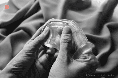 Primer plano en blanco y negro de dos manos sosteniendo una jaula de castidad de silicona transparente