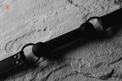 Primer plano en blanco y negro de una mordaza de bola negra en una correa de cuero remachada sobre piedra clara