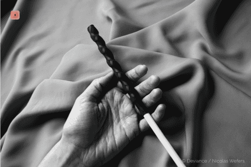 Fotografía en blanco y negro de una mano sosteniendo una vara con empuñadura de cuero trenzado sobre tela plegada