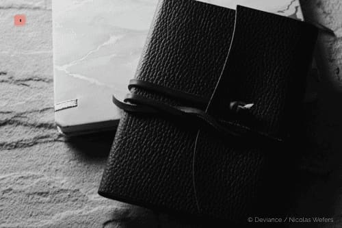 Fotografía en blanco y negro de un cuaderno de cuero granulado negro atado con un cordón de cuero, junto a una libreta jaspeada
