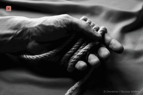 Primer plano en blanco y negro de una mano sujetando con holgura una cuerda áspera de cáñamo