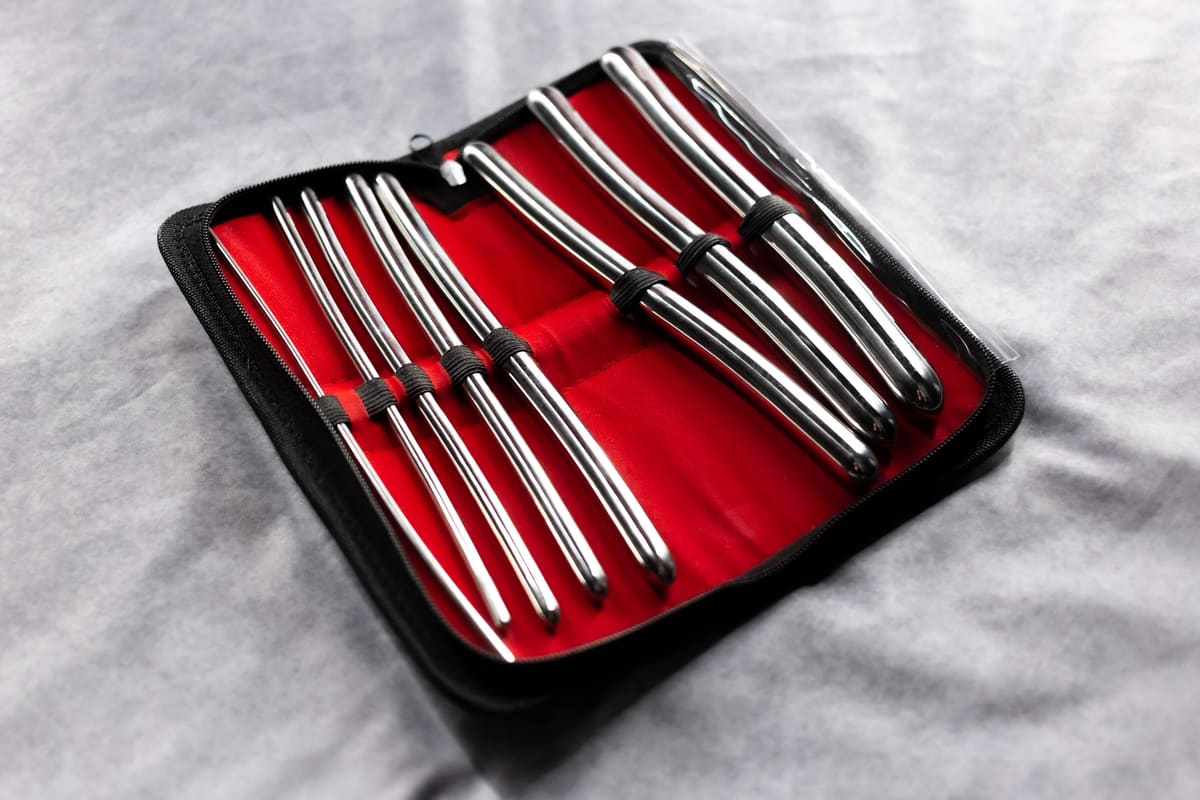 Estuche negro abierto con forro rojo que contiene ocho dilatadores de acero inoxidable de distintos grosores