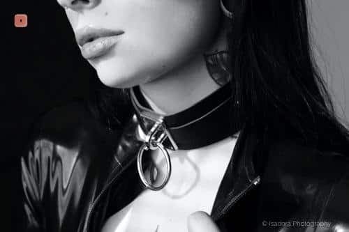 Primer plano en blanco y negro de un cuello con un collar de cuero estrecho con anilla en O, sobre una chaqueta de charol