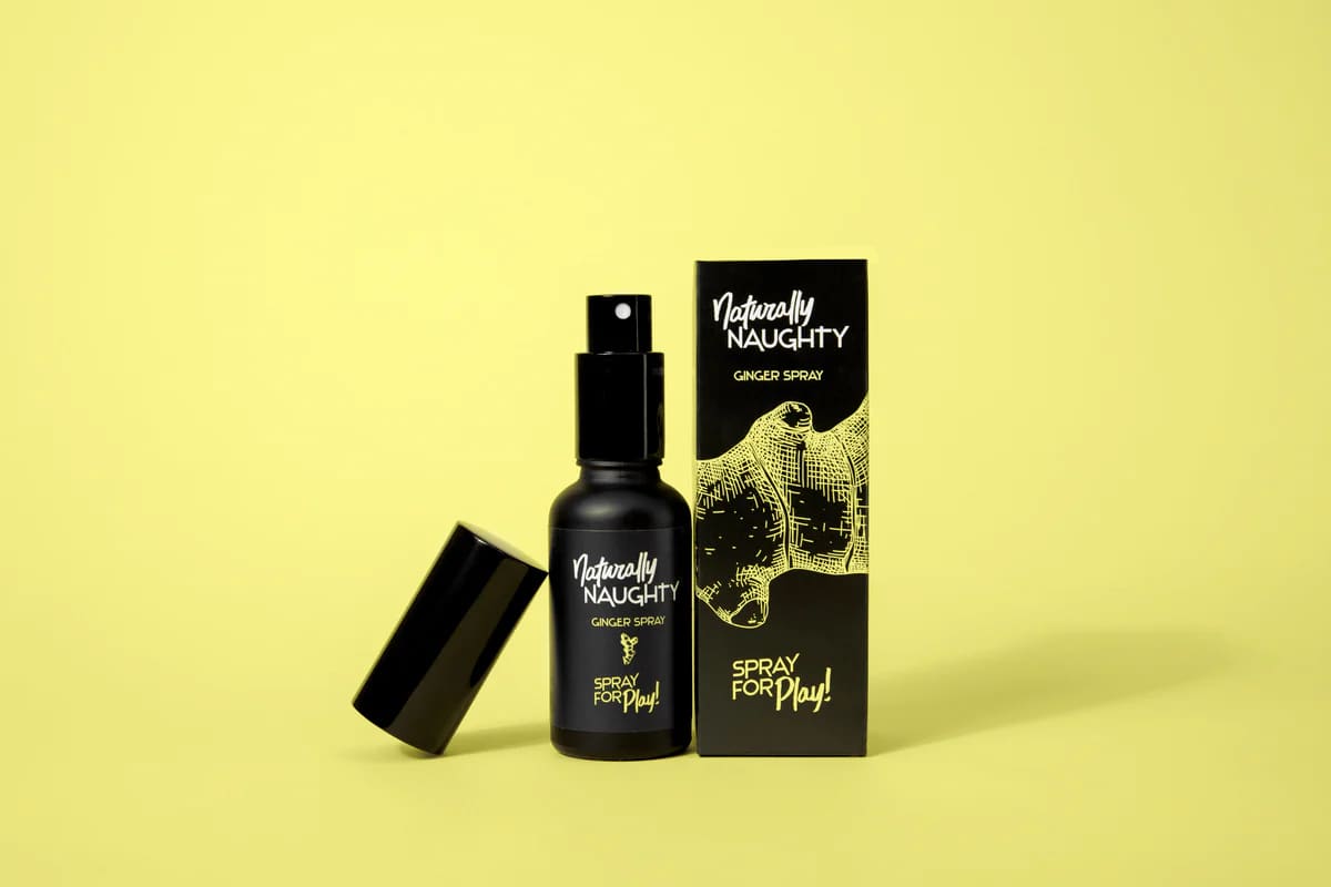 Frasco negro de «Naturally Naughty Ginger Spray» junto a su caja sobre fondo amarillo
