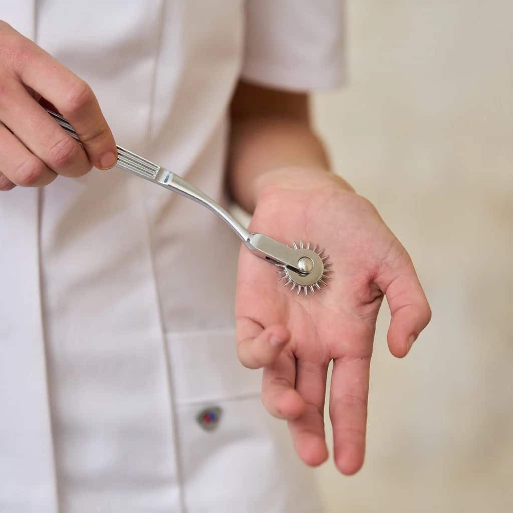 Persona con bata blanca pasa una rueda de Wartenberg por la palma abierta de otra persona
