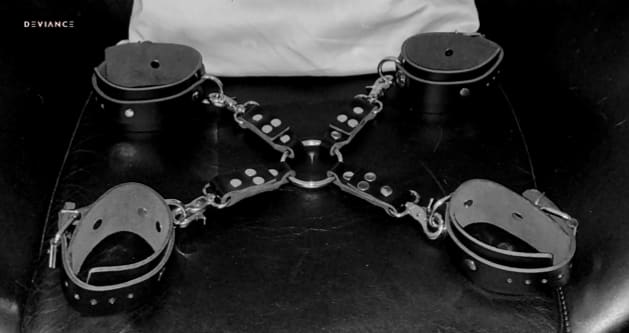Fotografía en blanco y negro de un set de ataduras completo dispuesto en estrella: cuatro muñequeras acolchadas unidas por cadenas a una anilla central