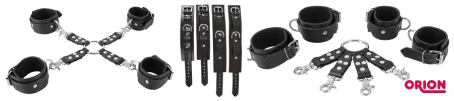 Vista de producto de un set de ataduras negro de Orion: esposas de muñeca y tobillo con remaches, una pieza de unión hogtie con anilla y cuatro correas con mosquetón