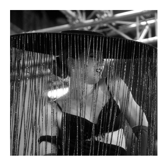 Fotografía en blanco y negro de una persona tras una cortina de cadenas brillantes en la feria