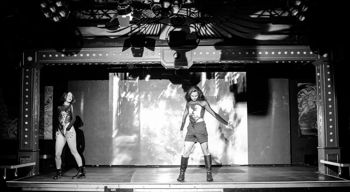 Fotografía en blanco y negro de la performance «here&now»: dos artistas ante una gran proyección en el KitKat Club