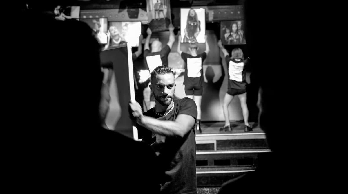 Fotografía en blanco y negro de la inauguración: Sahin Dellemann sostiene una copia ante la cámara mientras varios artistas alzan otras imágenes detrás