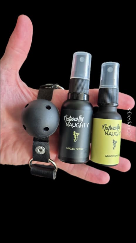 Una palma abierta sostiene una mordaza de bola negra con orificios de ventilación y dos frascos de «Naturally Naughty Ginger Spray»