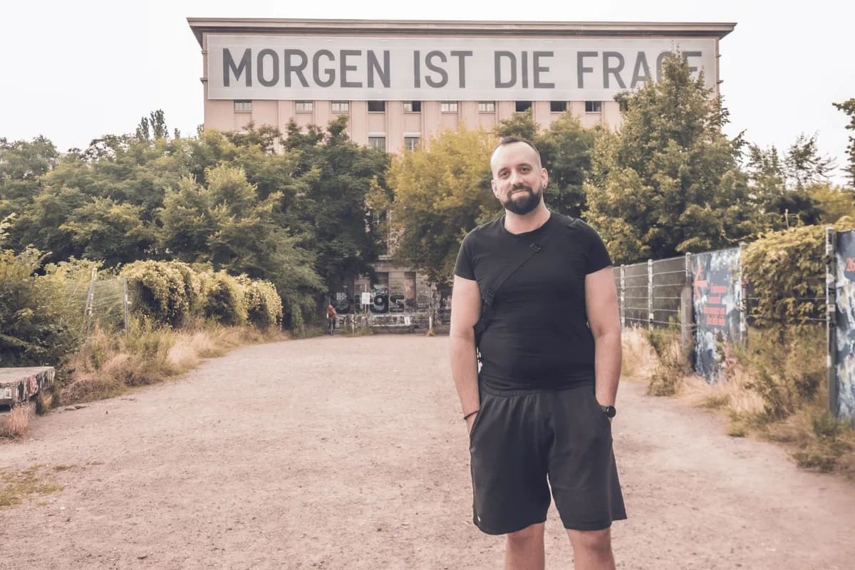 Persona con camiseta y pantalón corto negros frente al Berghain de Berlín, con el letrero «Morgen ist die Frage» en la fachada